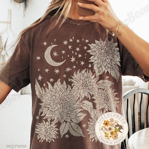 Pode incluir: Camiseta cor de caf&eacute; com um design celestial. O gr&aacute;fico inclui uma lua crescente, estrelas e grandes elementos florais em creme. A camisa tem um ajuste folgado e mangas curtas. O design &eacute; de "The Coco Bear Original Design".