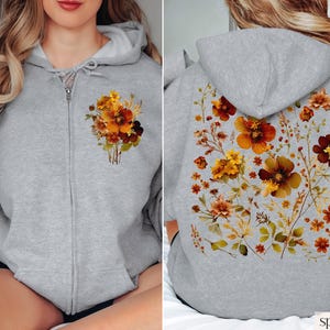 May include: A gray zippered hoodie with a floral print on the front and back. The flowers are in shades of orange, brown, and yellow. The hoodie is labeled "sport grey".