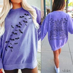 Op de afbeelding: Een paars sweatshirt met een zwart vleermuisontwerp aan de voorkant en een zwart spookhuisontwerp aan de achterkant. Het sweatshirt heeft een ontspannen pasvorm en een ronde hals.