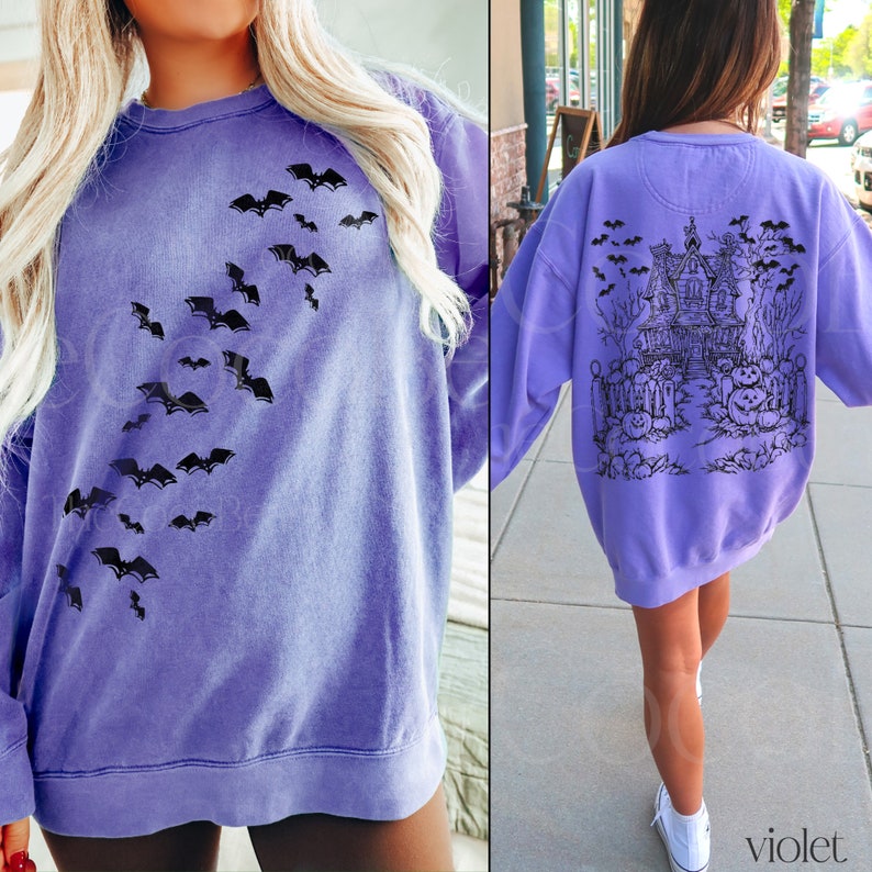 Op de afbeelding: Een paars sweatshirt met een zwart vleermuisontwerp aan de voorkant en een zwart spookhuisontwerp aan de achterkant. Het sweatshirt heeft een ontspannen pasvorm en een ronde hals.