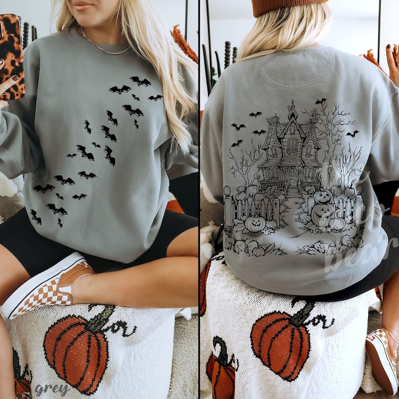 Op de afbeelding: Een grijs sweatshirt met een zwarte afbeelding van een spookhuis en vleermuizen op de rug. De voorkant van het sweatshirt heeft een zwarte afbeelding van vleermuizen die diagonaal vliegen.
