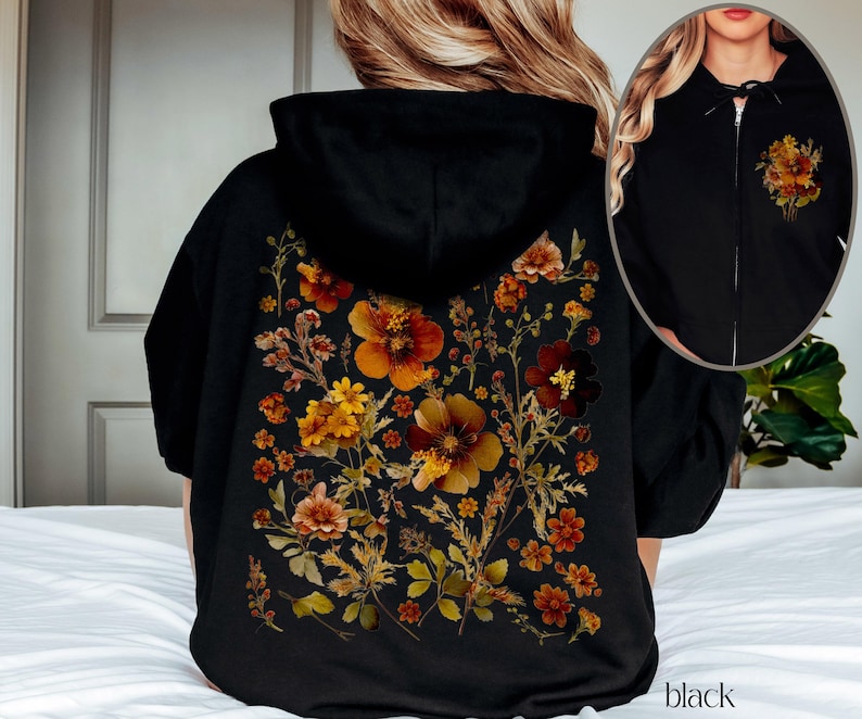 May include: Black hoodie with a zipper and a floral print on the back. The print features dried flowers in shades of orange, brown, and yellow.