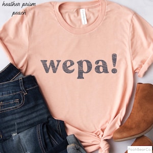 May include: A peach colored t-shirt with the word "wepa!" printed in black on the front.