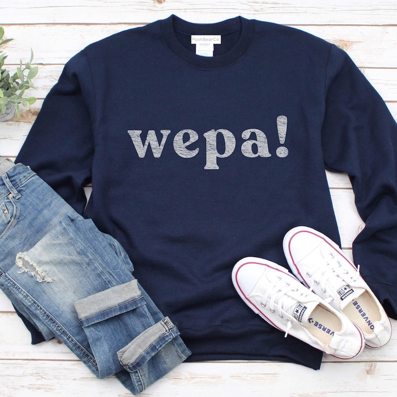 May include: A navy blue sweatshirt with the word "wepa!" printed in white on the front. The sweatshirt is paired with blue jeans and white sneakers.