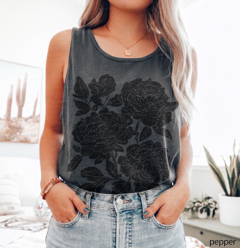 May include: A charcoal gray sleeveless tank top featuring a large black floral graphic print of peonies on the front. The garment has a round neckline and is paired with light blue denim jeans. The word pepper is printed in the bottom right corner.