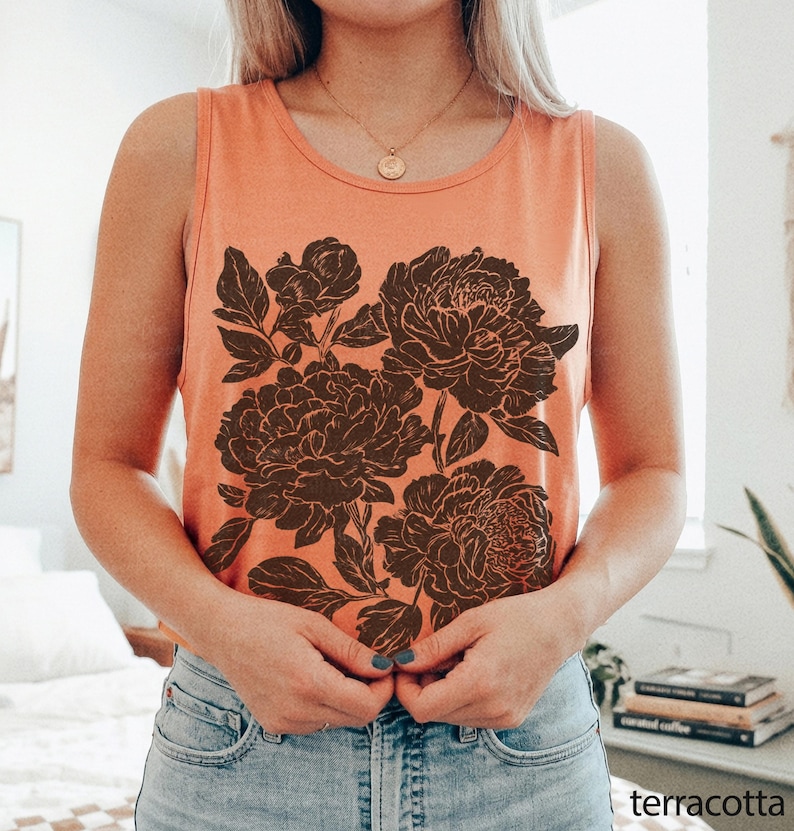 May include: A sleeveless tank top in a solid terracotta orange color featuring a large, dark brown graphic print of blooming peony flowers and leaves centered on the front. The garment has a round neckline and a relaxed, casual fit.