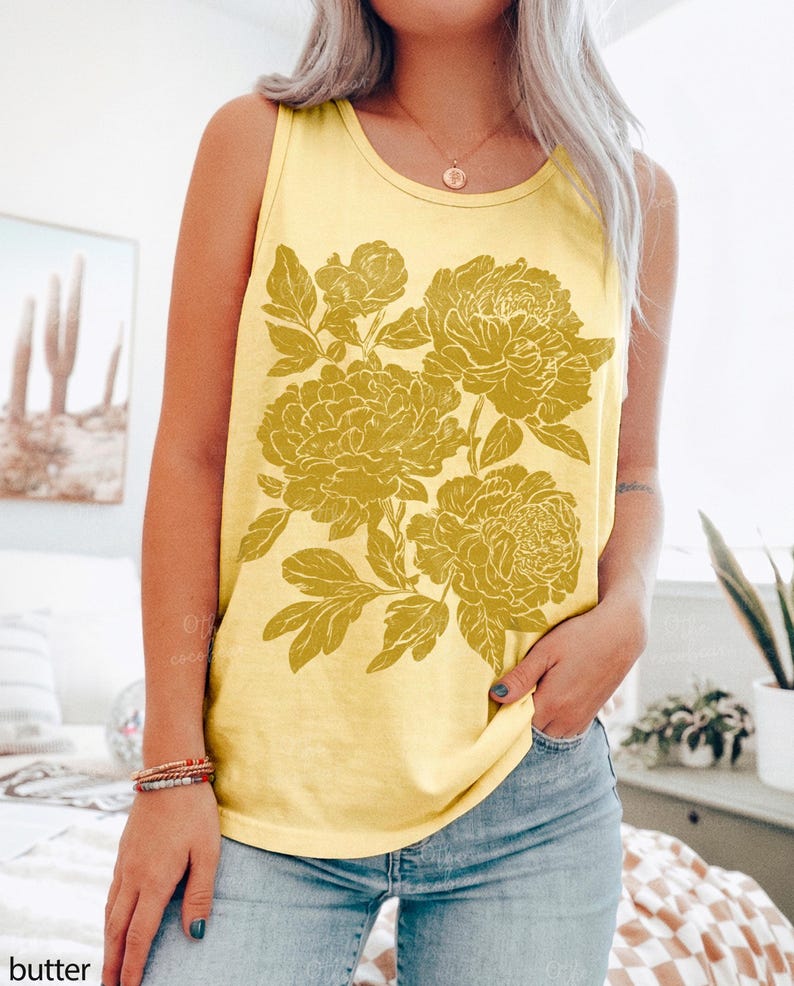 May include: A butter yellow sleeveless tank top featuring a large, detailed mustard yellow floral graphic print on the front. The design showcases multiple blooming flowers with intricate petals and leaves, centered on the chest of the garment.