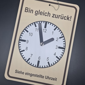 Könnte beinhalten: Ein beigefarbenes Schild mit braunem Rand und einer Kette, die oben hängt. Das Schild sagt "Bin gleich zurück!"  Es gibt ein Zifferblatt mit schwarzen Zeigern und schwarzen Zahlen auf weißem Hintergrund. Das Zifferblatt sagt "Siehe eingestellte Uhrzeit".