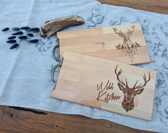 May include: Two wooden cutting boards with engraved deer designs. The top board has a geometric deer design with the text "Wild Kitchen" on the bottom board.