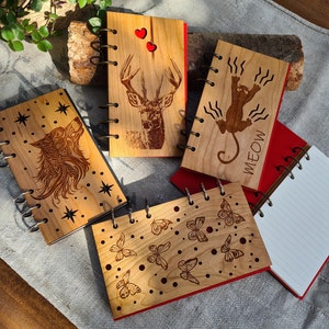 May include: Five wooden spiral bound journals with different designs. One features a wolf, another a deer, another a cat, another butterflies, and the last one is blank. All journals have red covers.