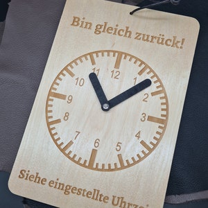 Op de afbeelding: Een houten bord met een klok en de tekst "Bin gleich zurück!" (Ik ben zo terug!) en "Siehe eingestellte Uhrzeit" (Zie ingestelde tijd).