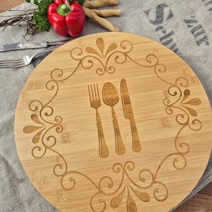 Puede incluir: Una bandeja redonda de servir de madera con un diseño decorativo de espirales y un tenedor, un cuchillo y una cuchara en el centro.