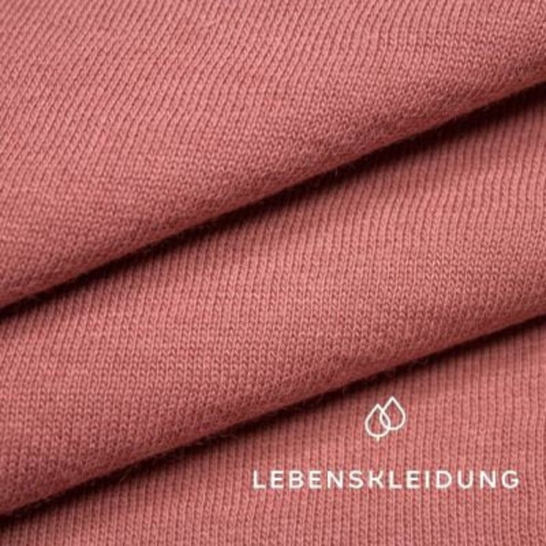 May include: Close-up of a soft, pink fabric with a ribbed texture. The fabric is folded in layers, revealing the texture and color. The text "LEBENSKLEIDUNG" is visible in the lower right corner of the image.