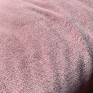 May include: Close-up of a soft, pink, textured fabric. The fabric has a slightly fuzzy appearance.