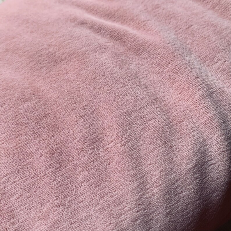 May include: Close-up of a soft, pink, textured fabric. The fabric has a slightly fuzzy appearance.