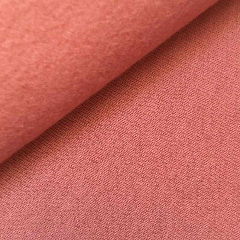 May include: Close-up of a soft, pink fabric with a textured surface. The fabric is folded in half, showing the inside and outside of the material.