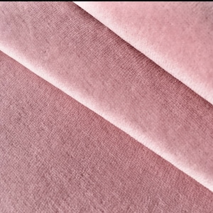 May include: Close-up of a soft, pink velvet fabric with a subtle texture. The fabric is folded in a way that shows the depth of the pile.