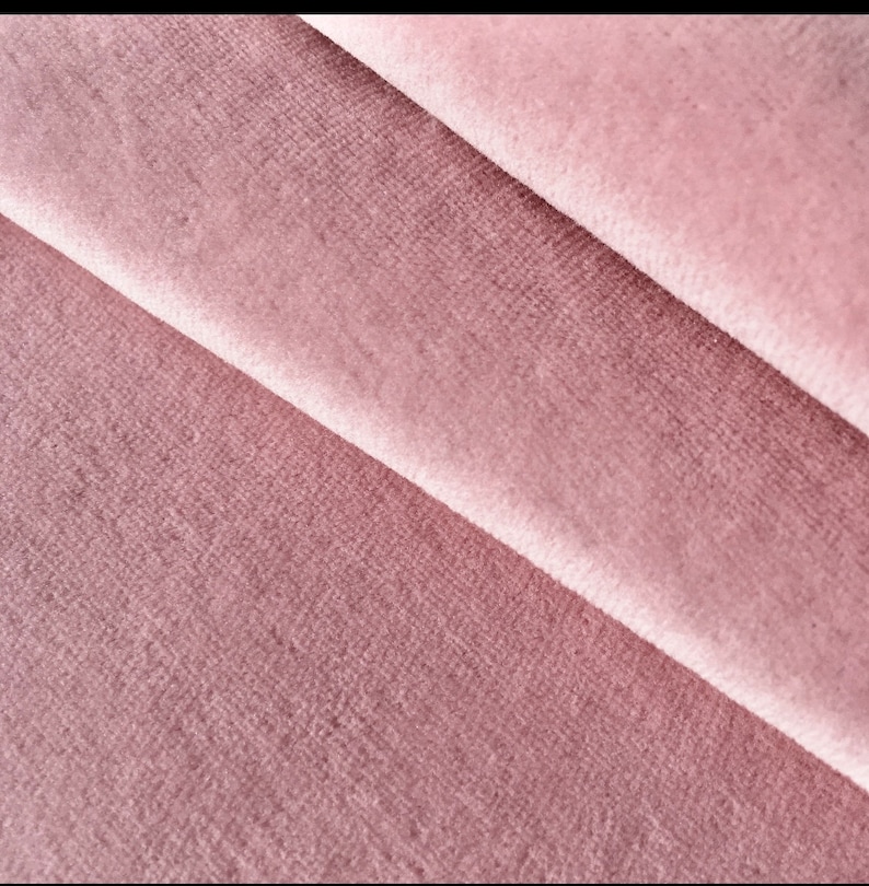 May include: Close-up of a soft, pink velvet fabric with a subtle texture. The fabric is folded in a way that shows the depth of the pile.