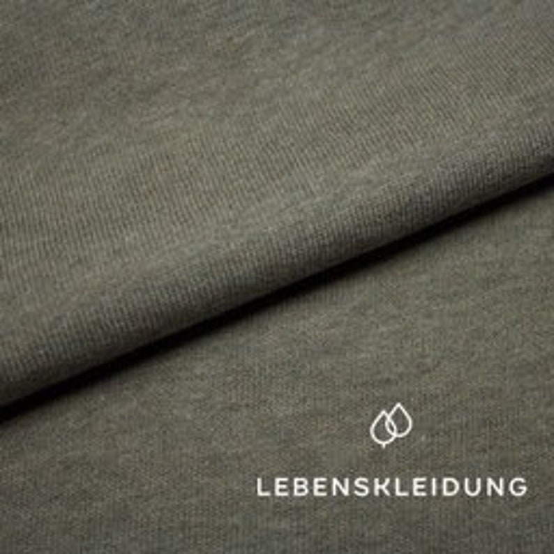 May include: Close-up of a soft, textured, green fabric. The fabric has a subtle ribbed texture and a slightly faded appearance.