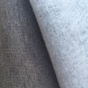 May include: Close-up of two fabric swatches. One is a dark gray knit fabric with a ribbed texture. The other is a light gray, fuzzy fabric.