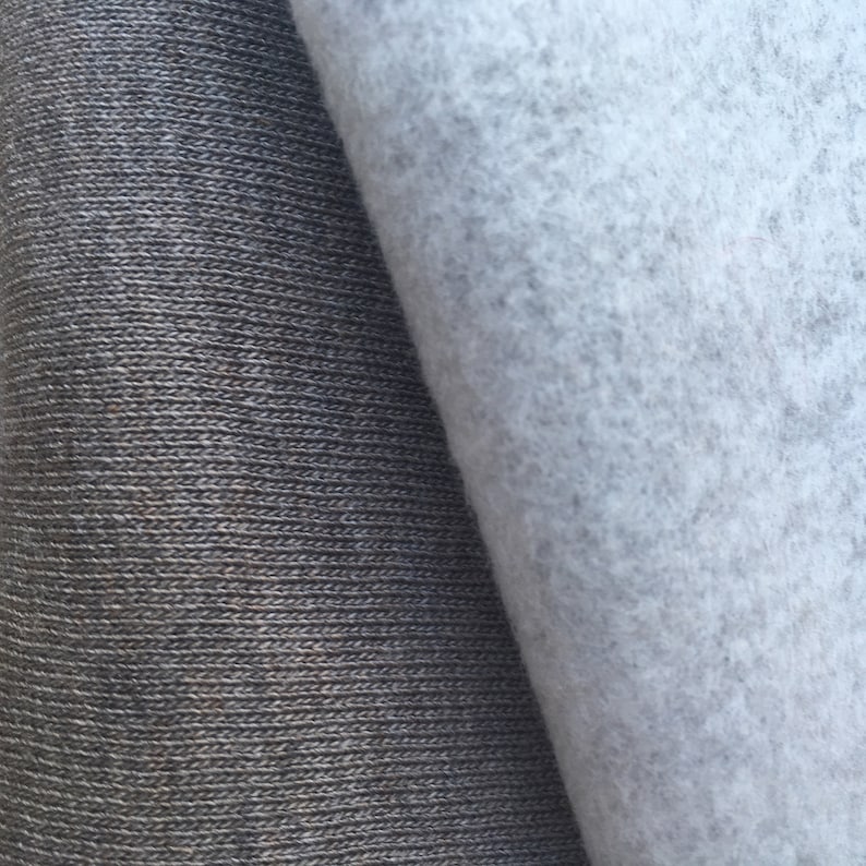 May include: Close-up of two fabric swatches. One is a dark gray knit fabric with a ribbed texture. The other is a light gray, fuzzy fabric.