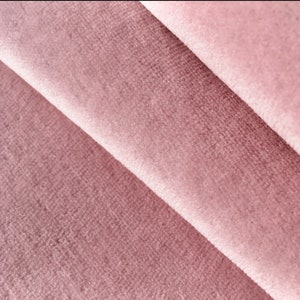 May include: Close-up of a soft, pink velvet fabric with a subtle texture. The fabric is folded in a way that shows the depth of the pile.