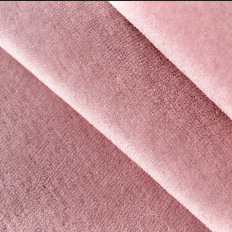 May include: Close-up of a soft, pink velvet fabric with a subtle texture. The fabric is folded in a way that shows the depth of the pile.