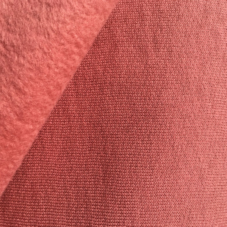 May include: Close-up of two different fabrics, one a soft, fuzzy fleece and the other a smooth, woven knit. Both fabrics are a deep reddish-brown color.