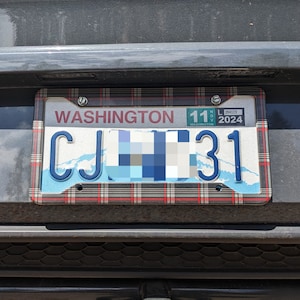 May include: A Washington state license plate with a decorative plaid frame. The plate displays the state name, the letters "CJ" and the numbers "31". The plate has a blue and white background with a wave design. The expiration date is November 2024.