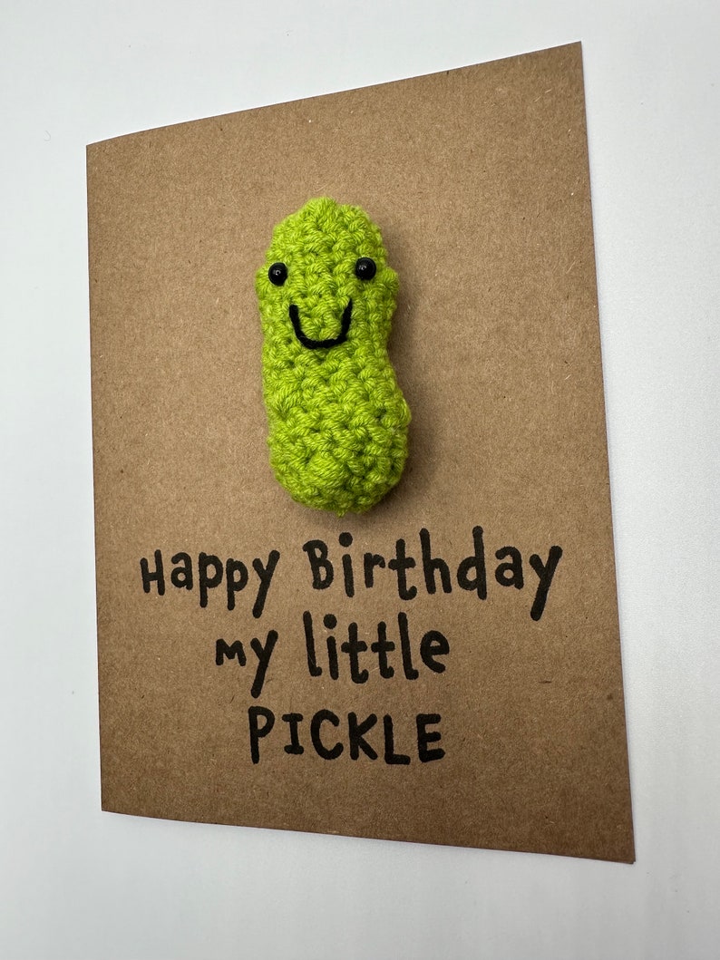 May include: A brown card with a green crocheted pickle with a smiling face. The card says "Happy Birthday my little PICKLE".