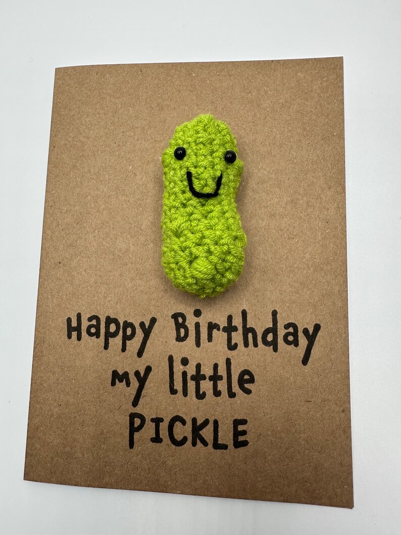 May include: A brown card with a green crocheted pickle with a smiling face. The card says "Happy Birthday my little PICKLE".
