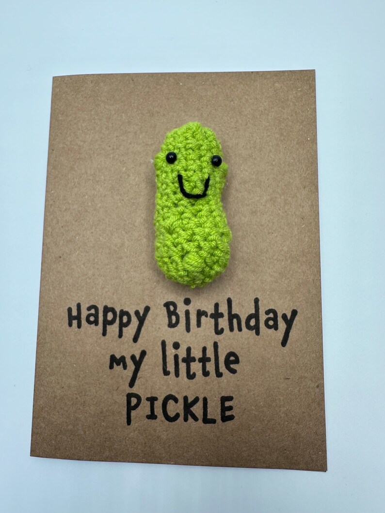 May include: A brown card with the text "Happy Birthday my little PICKLE" and a green crocheted pickle with a smiling face.