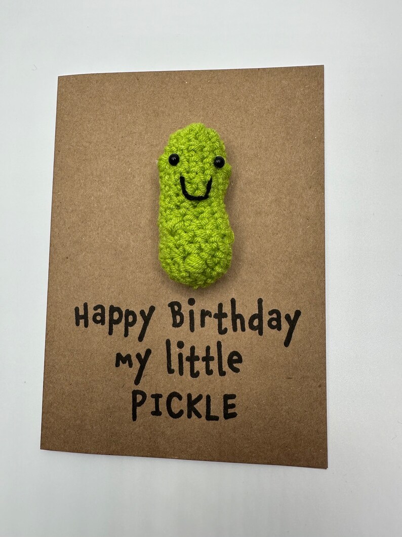 May include: A brown card with a green crocheted pickle with a smiling face. The card says "Happy Birthday my little PICKLE".