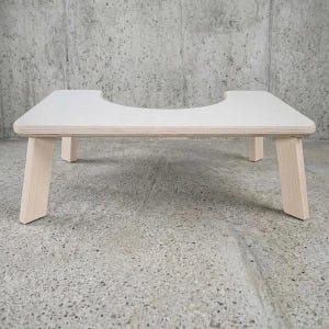May include: A low-profile wooden toilet stool featuring a smooth, white-finished top surface with a central U-shaped cutout. The stool is supported by four sturdy, light-coloured wooden legs that angle outward, providing a stable base for the structure.