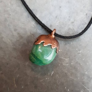 May include: A green stone pendant with a copper cap, hanging from a black cord.