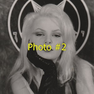 Puede incluir: Foto en blanco y negro de una mujer con cabello rubio que lleva un guante de cuero negro. Está posando con la mano en la barbilla. El fondo presenta un símbolo en blanco y negro con un pentagrama.