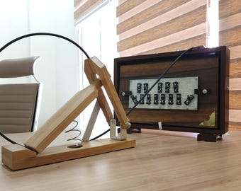 以下が含まれることがあります： バネ仕掛けのアームを備えた木製の機械装置で、黒いケーブルで長方形の木箱に接続されています。木箱の中央パネルには、C、D、E、F、G、A、B、Cの音符が白い文字で記された黒いボタンが配置されています。