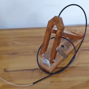 以下が含まれることがあります： 黒いケーブルとバネが付いた木製ギター弦巻き。巻き取り機は薄い茶色の木でできており、ネジが付いた金属プレートがあります。