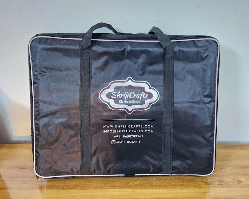 May include: A black rectangular carrying case with two top handles and a zipper closure. The front features a white logo with the text ShrijiCrafts The Art collection, along with website, email, phone number, and social media handle information.