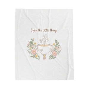 May include: White blanket with a floral design and the text "Enjoy the Little Things." The illustration features a teacup held by hands, with steam shaped like hearts, surrounded by flowers and greenery.
