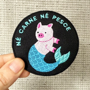 Peut inclure: Un patch brodé noir avec une sirène cochon rose avec une queue bleue et le texte "Nè carne nè pesce".