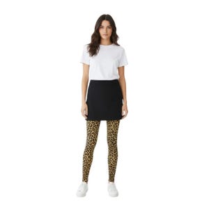 A woman standing, wearing a white t-shirt, black mini skirt, black high heels, and mustard coloured leopard print patterned tights.