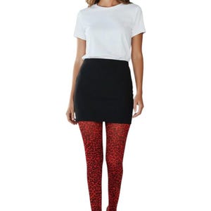 A woman standing, wearing a white t-shirt, black mini skirt, black high heels, and bright red leopard print patterned tights.