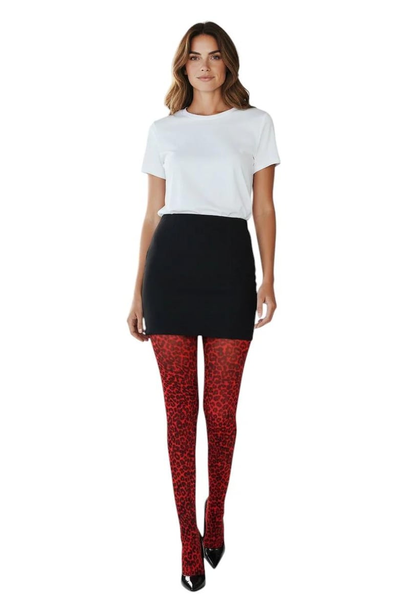 A woman standing, wearing a white t-shirt, black mini skirt, black high heels, and bright red leopard print patterned tights.
