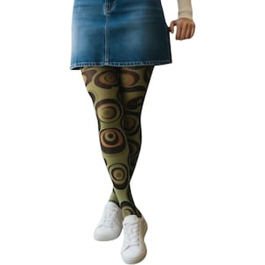 Può includere: Una gonna di jeans abbinata a collant verde oliva con un motivo circolare retrò marrone e arancione. Le scarpe da ginnastica bianche completano l'outfit, creando un look elegante e unico.