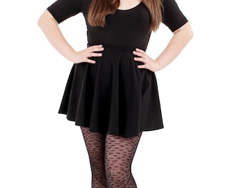 May include: A woman wearing a black skater skirt, black top, and black patterned tights with black heels.