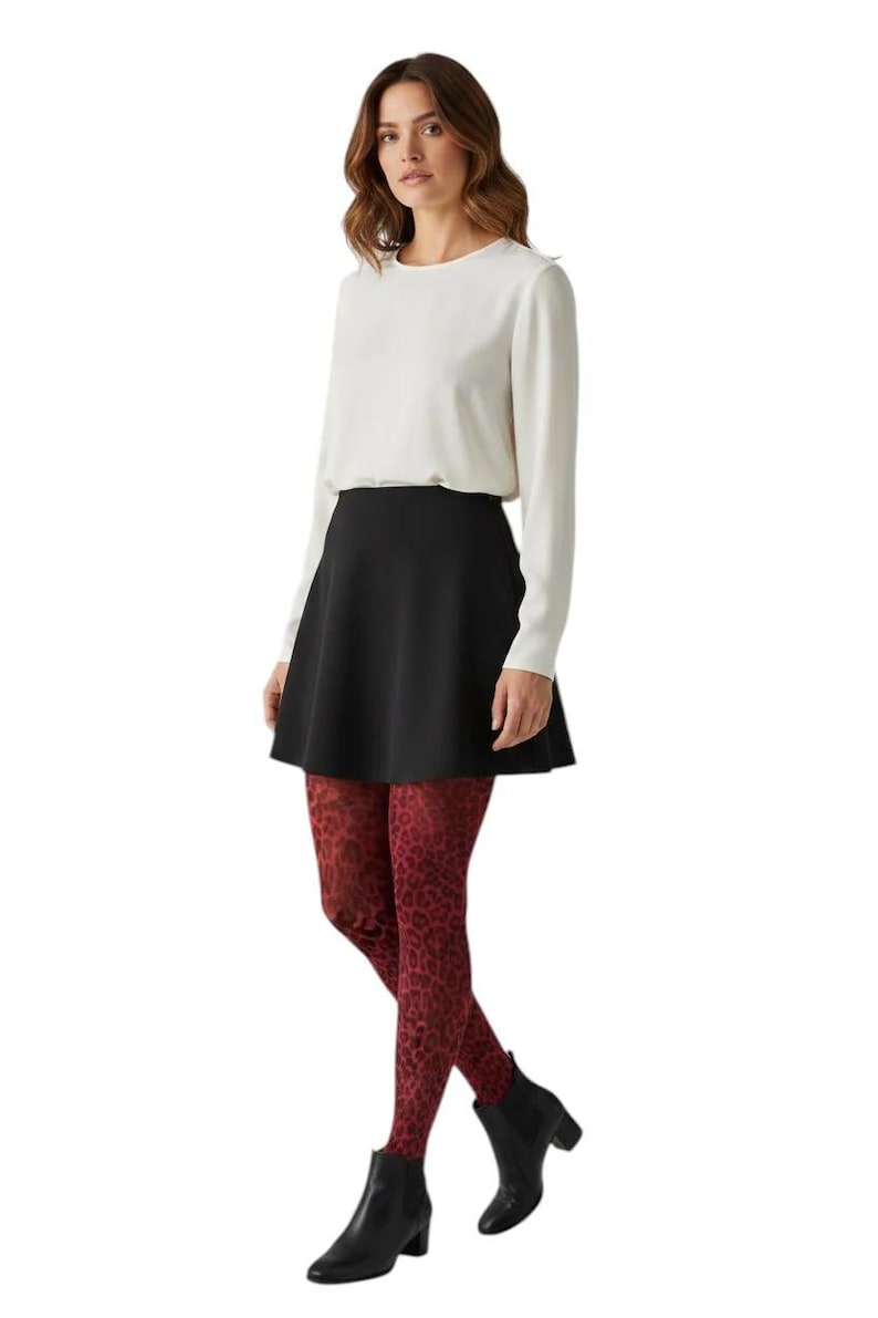 A woman standing, wearing a white long-sleeved top, black mini skirt, black ankle boots, and dark burgundy leopard print patterned tights.