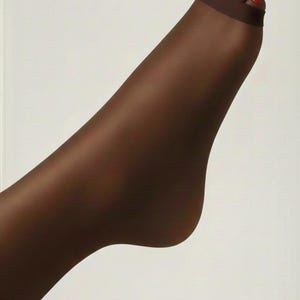 May include: A close-up of a leg wearing sheer, dark brown hosiery. The foot is angled, with red nail polish on the toes. The hosiery has a dark band around the ankle.
