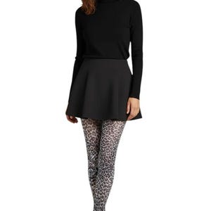 A woman standing, wearing a black turtleneck top, black mini skirt, black high heels, and white and grey monochrome leopard print patterned tights.
