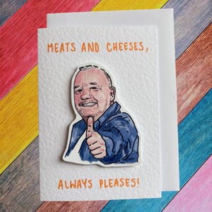 May include: A white greeting card featuring a cartoon illustration of a man giving a thumbs up. The text "MEATS AND CHEESES, ALWAYS PLEASES!" is written in orange. The background has a striped pattern.